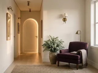 Corredor de casa residencial com porta em arco iluminada, poltrona ameixa e vaso com eucalipto