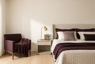 Quarto individual arrumado com colcha de algodão, abajur de latão e vaso pequeno com folhagem